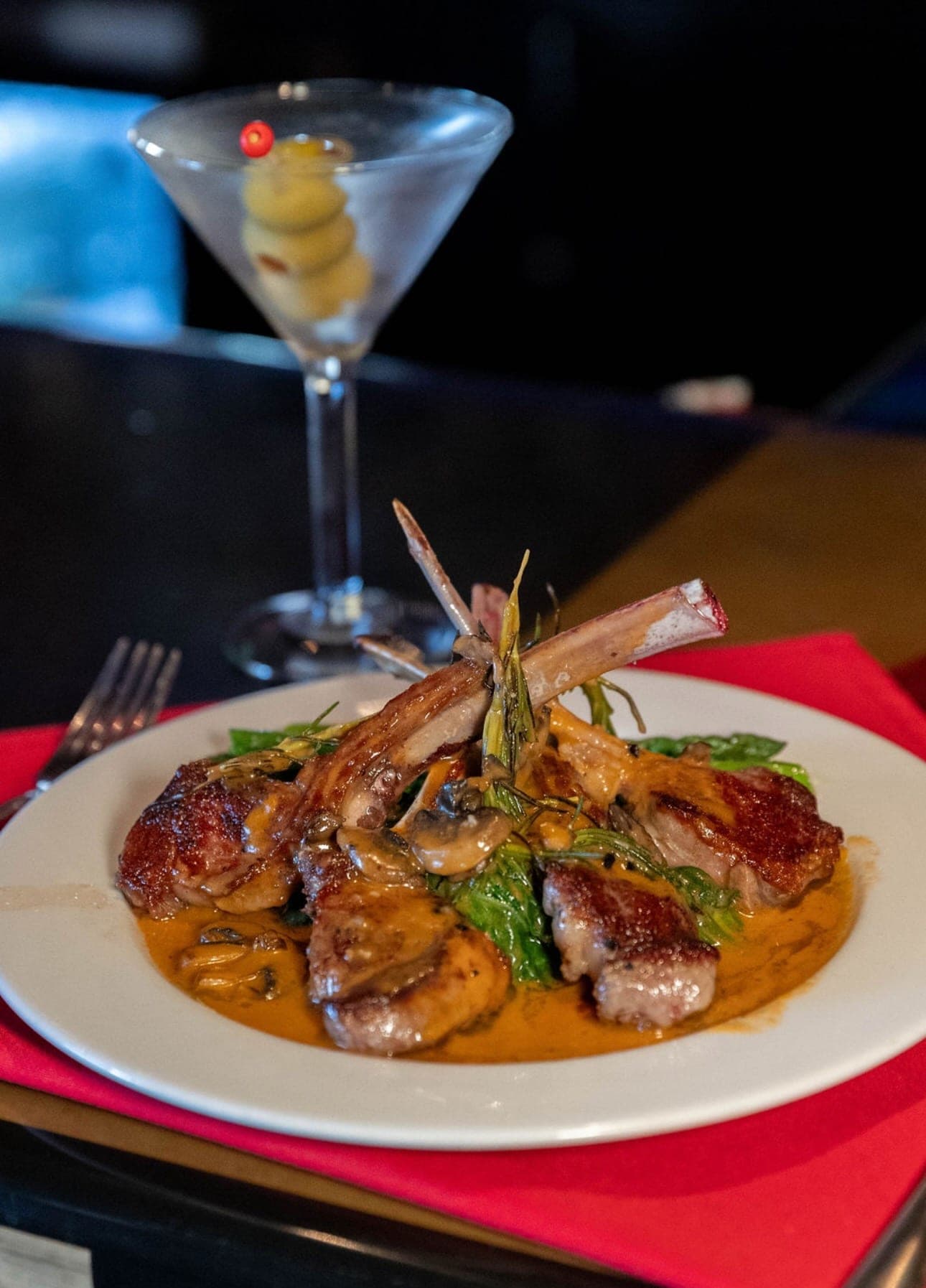 Pan-seared lamb chops in a rosemary cream sauce beside a martini at Nick's Italian.